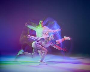 Portrait of young girls dancing hip-hop isolated over gradient blue purple background in neon with mixed light. Performance