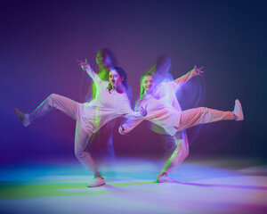 Portrait of young girls, friends dancing hip-hop isolated over gradient blue purple background in neon with mixed light.