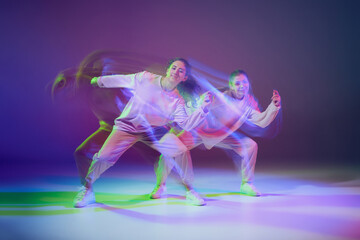 Obraz premium Portrait of young girls dancing hip-hop isolated over gradient blue purple background in neon with mixed light. Energy burst