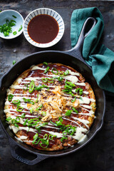 Okonomiyaki or the Japanese savory pancake filled with cabbage and served with spring onion and katsuboshi