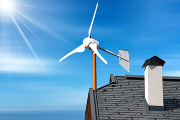 Close-up of a small wind turbine on the top of a roof of a house, against a blue sky with clouds...