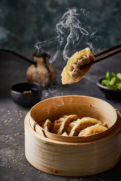 Gyozo with steam coming of. Steaming basked underneath with more gyoza.