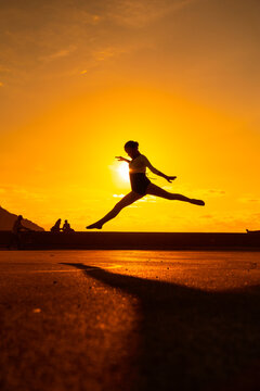 Young woman dancer performing a jump along the beach at sunset