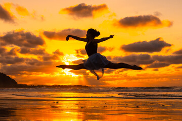 Fototapeta na wymiar Young dancer on the beach at sunset performing a jump with the sea in the background