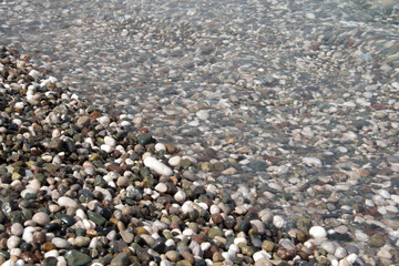 Small colorful pebbles and water. The beach is made of pebbles, the seashore, small colored pebbles in the water.