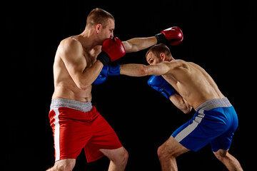 Fototapeta na wymiar Fight. Dynamic portrait of two professional boxer in sports uniform boxing isolated on dark background. Concept of sport, competition, training, energy.
