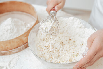 Food preparations. Little girl wearing an apron in the kitchen. Mixing dough to make cookies. Baking ingredients for shortcrust pastry. Close up, selective focus