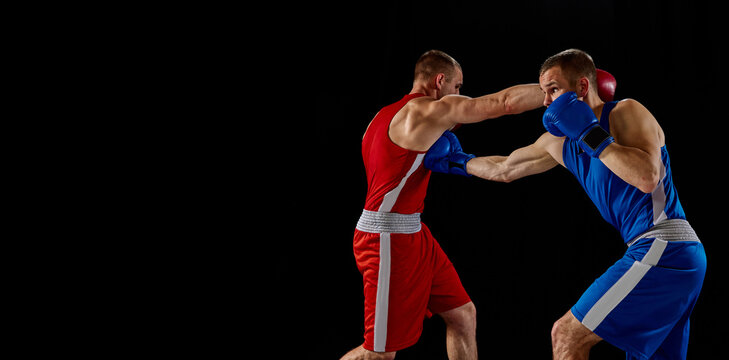 Male professional boxers in blue and red sports uniform practicing punch isolated on dark background. Concept of sport, competition, training, energy. © master1305
