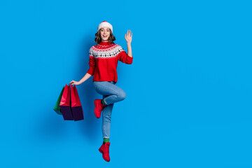 Fototapeta na wymiar Full length portrait of excited girl jumping hold packages arm palm waving empty space isolated on blue color background