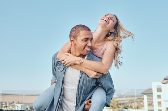 Interracial, couple and piggy back with outdoor fun of a happy girlfriend and boyfriend feeling love. Happiness of a woman and man together for anniversary or engagement announcement with a smile - Powered by Adobe