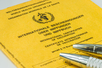 World Health Organization yellow vaccination book and two ballpoint pens. Cover sheet of the yellow...
