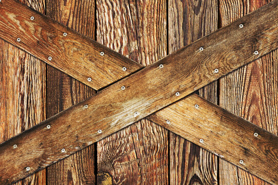 Wooden barn door. X shape wooden desks. Rustic nails vintage desk construction background. Countryside architecture texture. Village building farm door entrance.