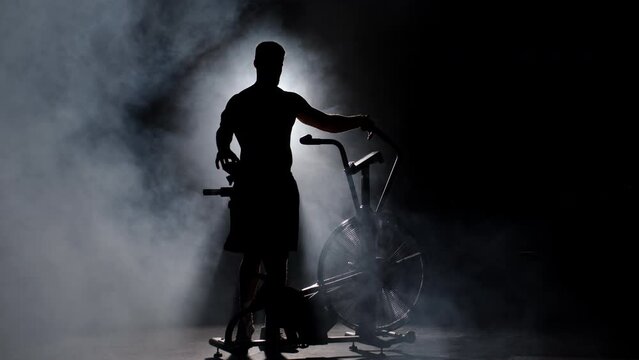 Sportive Athletic Male Has Fast Training on Stationary Bike .