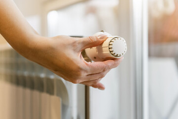 A woman's hand turns the battery heating knob. Start of the heating season. The concept of home heating of an apartment or house