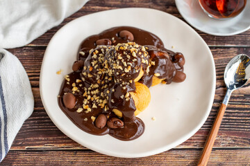 Profiterole dessert on wood background. Traditional french cuisine delicacies. Profiterole dessert topped with chocolate and hazelnut pieces. close up