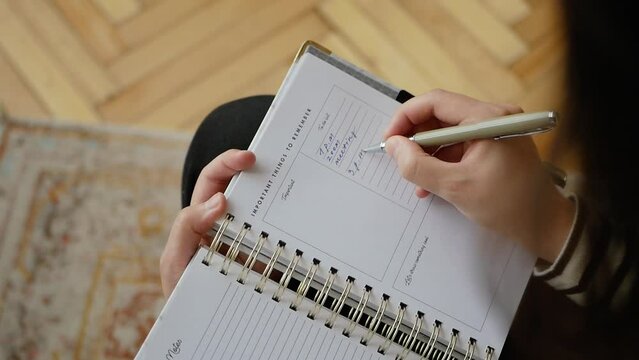 Woman is writing down a schedule in her agenda paper book.