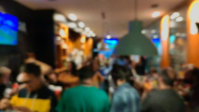 many people eat snacks and drink socializing, talking and enjoying inside a busy bar with music at the end of the work week at night, unfocused blocked shot, Ordes, Galicia, Spain