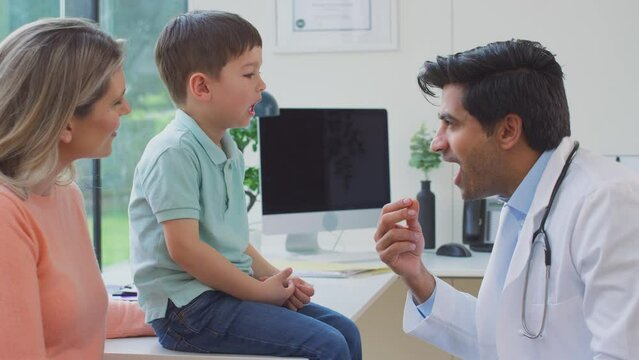 Male doctor or GP wearing white coat examining boy looking at mouth and throat - shot in slow motion