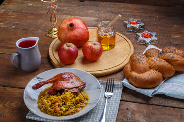 Spelled with vegetables and duck leg in a plate next to challah, wine, honey and apples