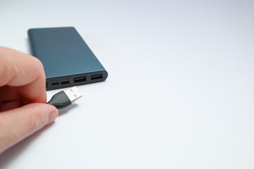 Hand holding USB cable and grey power bank. Hand connecting USB cable to the powerbank.