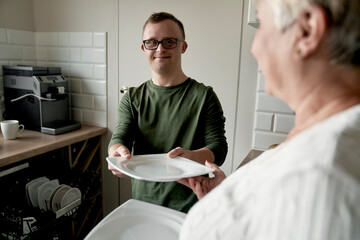 Caucasian adult man with down syndrome and his mother unloading dish washer at home