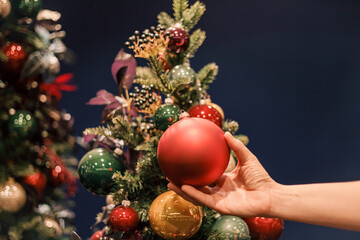 Red decorative Christmas ball in the hands of a woman decorating her Christmas tree