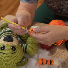 A woman has a crochet hook in her hands. She knits amigurumi toys.