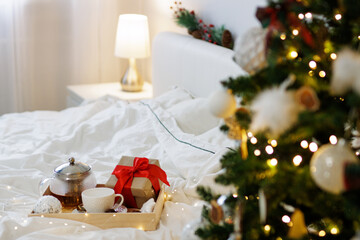 Christmas concept - wooden tray with coffee or tea mug and gift box in decorated bedroom with Christmas tree