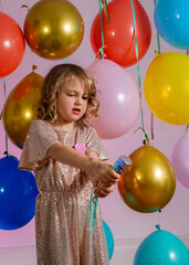 Young girl in a sparkly party outfit blowing up the confetti сannon. Balloons on the background.