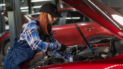 A woman auto mechanic in overalls is repairing a car.