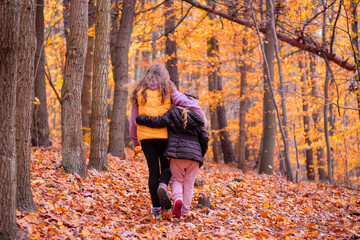 Two girls (sisters) on a walk in a beautiful autumn forest. Shallow depth of field.