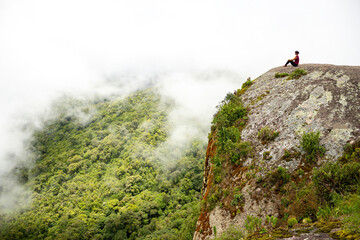 Person woman on round stone overlooking nature Atlantic forest after trail through the woods. Located in the village of Monte Verde, Minas Gerais.