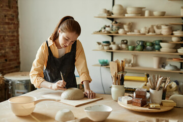 Warm toned portrait of young female artist shaping handmade ceramic bowl in pottery studio, copy space - obrazy, fototapety, plakaty