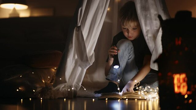 little boy reads book at night, lighting by lantern sitting in tent in bedroom