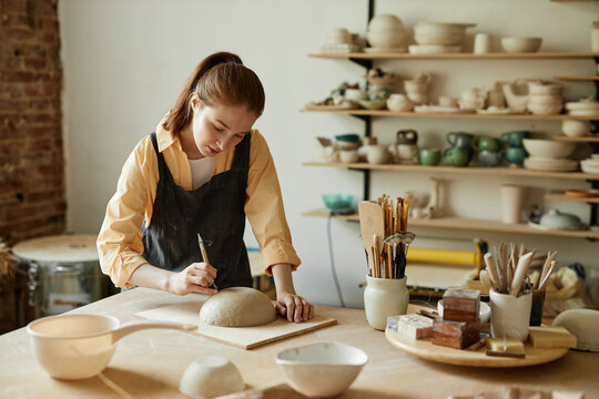 Warm toned portrait of young female artist shaping handmade ceramic bowl in pottery studio, copy space