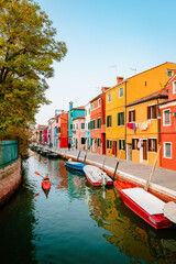 Characteristic Burano street with canal and canoes of tourists and colorful houses at sunset