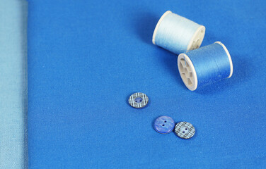 Blue background with spools of thread and buttons. Accessories for sewing.