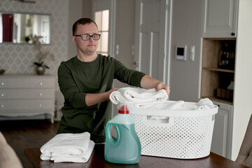 Caucasian adult caucasian man with down syndrome folding the laundry