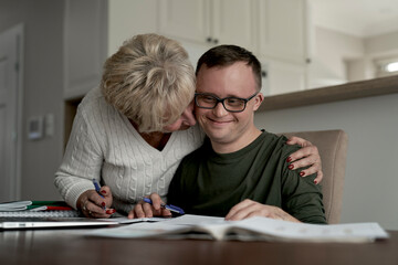 Mother hugging caucasian man with down syndrome while learning at home