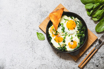 green shakshuka in a cast iron skillet. fried eggs with spinach and fried toast. healthy nutritious breakfast