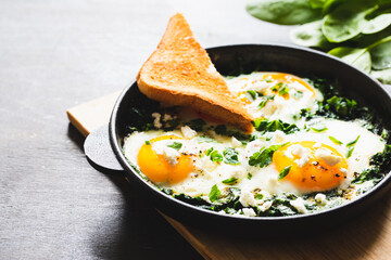 green shakshuka in a cast iron skillet. fried eggs with spinach and fried toast. healthy nutritious breakfast