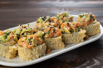 Japanese tempura hot sushi roll on white plate on wooden background. Sushi pieces with salmon, cucumber, cream cheese, avocado wrapped in crunchy seaweed