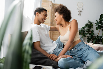 sexy african american couple sitting on bed and smiling at each other on blurred foreground.