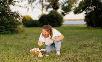 Teenage girl teasing dog and playing with it on grass. Teenager making gesture and making face to pet