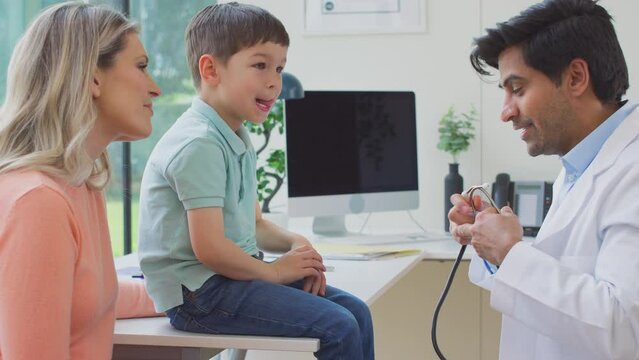 Male doctor or GP wearing white coat examining boy listening to chest with stethoscope before giving him high five and fist bump - shot in slow motion