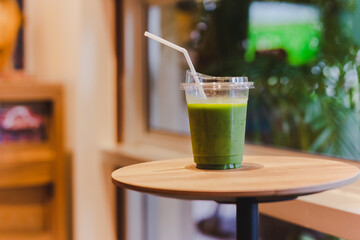 Green smoothie in plastic glass with straw on wooden table in cafe.