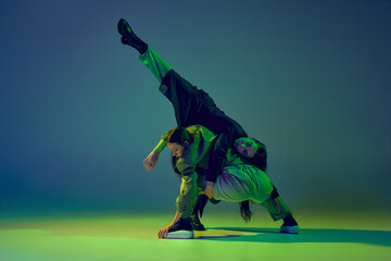 Modern dance concept. Energetic couple of two young woman dancing contemporary dance on gradient blue-green background in neon light. Concept of art, creativity, movement, style and fashion, action.