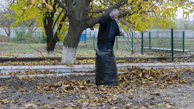 Seasonal raking of leaves in the garden. The concept of cleaning and caring for the garden. A man rakes faded and colorful leaves in the garden. Autumn cleaning before winter
