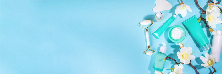 Spring face skin care, hand care cosmetic in unbranded containers, bottles, tubes with spring flower twigs on light blue turquoise background. Spring hand skin care cosmetics background top view copy 