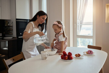 An image of a young woman and her little cute daughter are cooking in the kitchen. Have fun...